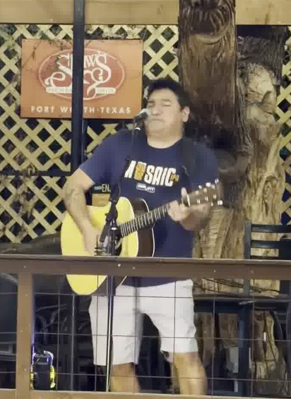Tom Reyes performing acoustic guitar at an open mic in Fort Worth