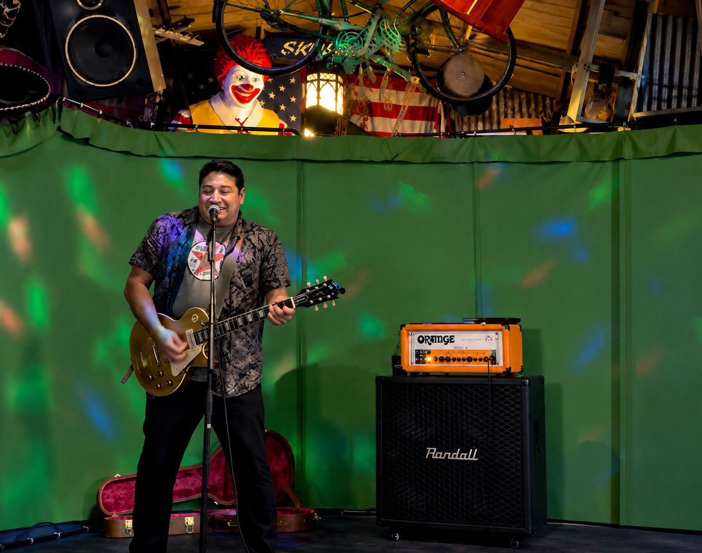 Tom Reyes performing live with electric guitar under a green stage backdrop
